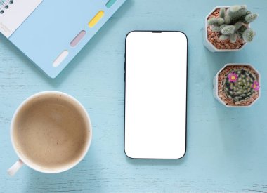 Üst düzey kompozisyon, konsept online alışveriş, blog, logo, ürün ve sosyal medya. Düz ekran cep telefonu modeli mavi arka planda ve kahve fincanı, kaktüs, defter