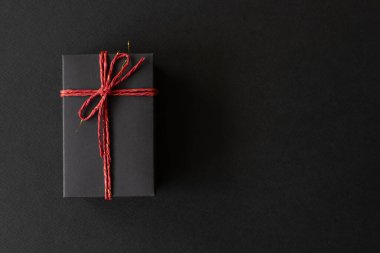Üst manzara, siyah hediye kutusu siyah kağıtta kırmızı bir iple bağlanmış. Doğum günü konsepti için hediye kutusu, teşekkürler, tebrikler, anneler günü, yıldönümü, sevgililer günü.