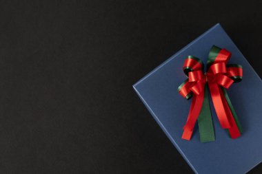 Üst manzara, siyah arka planda kırmızı ve yeşil fiyonklu mavi hediye kutusu düzlüğü. Tatil kavramı.