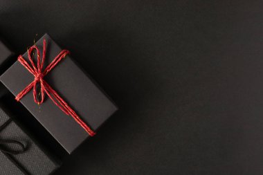 Üst manzara, siyah hediye kutusu siyah kağıtta kırmızı bir iple bağlanmış. Doğum günü konsepti için hediye kutusu, teşekkürler, tebrikler, anneler günü, yıldönümü, sevgililer günü.