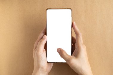 El ele tutuşan akıllı telefon, kahverengi arka planda beyaz bir ekran gösteriyor. Üst manzara, fotokopi alanı olan düz bir yer. Çevrimiçi iş, blog yazarı ve reklamcılık kavramı