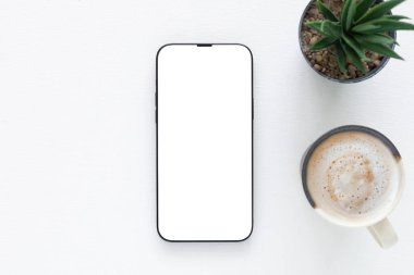 Düz konum, beyaz ekran ve seramik kahve ile modern akıllı telefon minimalist bir kapta sulu bitki. Teknoloji, yaşam tarzı veya çalışma alanı için ideal.