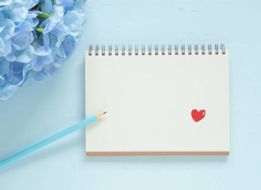 Üst manzara, kırmızı kalp şekli defterin ve kalemin sayfasında mavi ahşap arka planda mavi ortanca var. Teziniz için boşluk