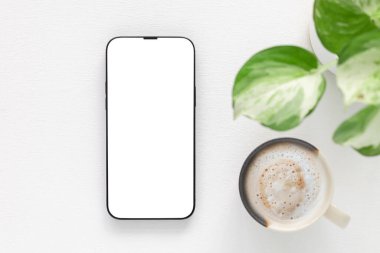 Konsept alışverişi, blog, logo, ürün ve sosyal medya. Üst manzara, düz bir düz telefon, beyaz ekran ve kahve fincanı olan, beyaz arka planda bitki yetiştiren modern bir akıllı telefon. Teknoloji, yaşam tarzı. 