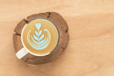 Üst manzara, bir cappuccino, beyaz ve kahverengi benekli seramik bardakta, ahşap kırsalda oluşturulan beyaz köpüklü bir kalp şeklinde latte sanatı içerir. Afiş, kafe ya da kahve adamı kavramı