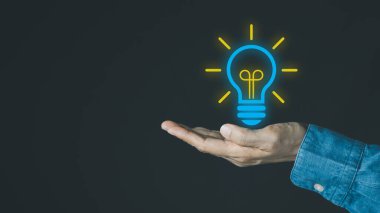 Sarı ışınlı, parlayan mavi bir ampulün grafiğini gösteren bir elin yakın çekimi. Düşüncenin gücü ve yenilikçi stratejiler üretimi. Yenilik ve yaratıcılık kavramı