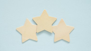 Üç basit ahşap yıldız açık mavi bir arka planda yan yana dizilir. Sıralama sistemi. Ortalama kaliteyi, iyi müşteri geribildirimini ya da dengeli bir değerlendirmeyi sembolize edebilir.