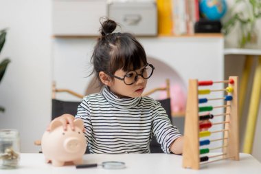 Cute asian child girl putting money into piggy bank to save money for the future clipart