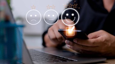 Müşteri hizmetleri değerlendirme konsepti. Akıllı telefon kullanmak, sanal ekranda gülümseyen yüz ifadelerine basmaktır..