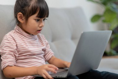 Asyalı liseli kız evdeki kanepede tek başına otururken dizüstü bilgisayar kullanıyor. Çocuk çevrimiçi sosyal medya içeriğini okumayı öğreniyor, eğitim dersleri alıyor arkadaşlarla sohbet ediyor. Çocuklar teknoloji bağımlılığı