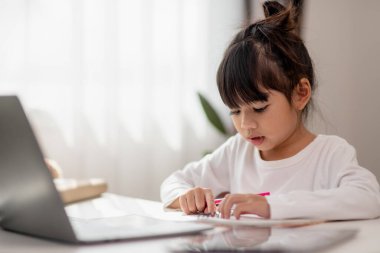 Asyalı liseli kız evde dizüstü bilgisayarla ödevini yapıyor. Çocuklar çalışmak için aletler kullanırlar. Çocuklar için eğitim ve uzak mesafe eğitimi. Karantina sırasında evde eğitim. Evde kal.