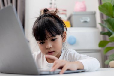 Asyalı liseli kız evde dizüstü bilgisayarla ödevini yapıyor. Çocuklar çalışmak için aletler kullanırlar. Çocuklar için eğitim ve uzak mesafe eğitimi. Karantina sırasında evde eğitim. Evde kal.