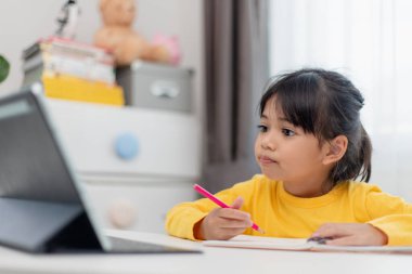 Asyalı liseli kız evde dijital tabletle ödevini yapıyor. Çocuklar çalışmak için aletler kullanırlar. Çocuklar için eğitim ve uzak mesafe eğitimi. Karantina sırasında evde eğitim. Evde kal.