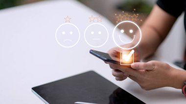 Müşteri hizmetleri değerlendirme konsepti. Akıllı telefon kullanmak, sanal ekranda gülümseyen yüz ifadelerine basmaktır..