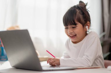 Asyalı liseli kız evde dizüstü bilgisayarla ödevini yapıyor. Çocuklar çalışmak için aletler kullanırlar. Çocuklar için eğitim ve uzak mesafe eğitimi. Karantina sırasında evde eğitim. Evde kal.