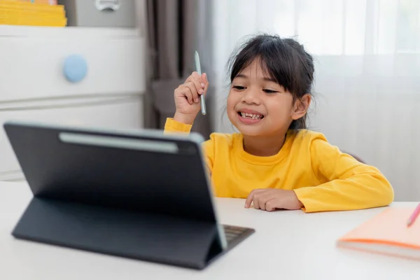 stock image Asian schoolgirl doing her homework with digital tablet at home. Children use gadgets to study. Education and distance learning for kids. Homeschooling during quarantine. Stay at home