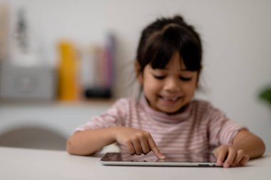 Asyalı küçük tatlı kız masadaki dijital tablet ekranına dokunuyor. 