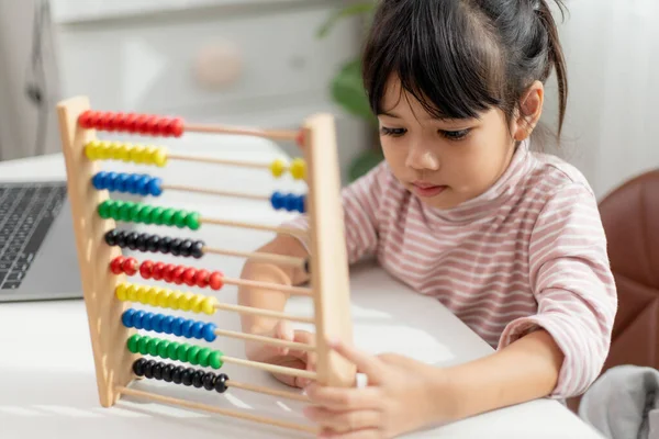 一个年轻可爱的亚洲女孩正在用一个戴着彩色珠子的算盘来学习如何在家里数数 — 图库照片