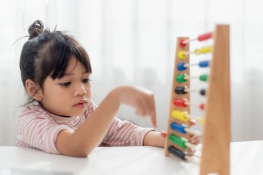Genç ve tatlı bir Asyalı kız abaküsü renkli boncuklarla evde saymayı öğrenmek için kullanıyor.
