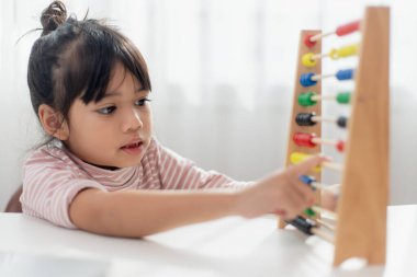 Genç ve tatlı bir Asyalı kız abaküsü renkli boncuklarla evde saymayı öğrenmek için kullanıyor.