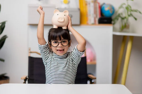 Little Asian girl saving money in a piggy bank, learning about saving, Kid save money for future education. Money, finances, insurance, and people concept