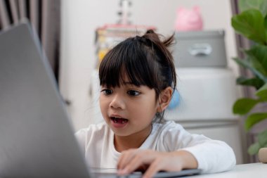 Asyalı liseli kız evde dizüstü bilgisayarla ödevini yapıyor. Çocuklar çalışmak için aletler kullanırlar. Çocuklar için eğitim ve uzak mesafe eğitimi. Karantina sırasında evde eğitim. Evde kal.