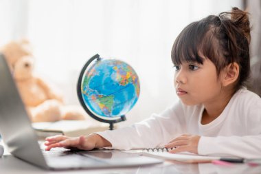 Asyalı liseli kız evde dizüstü bilgisayarla ödevini yapıyor. Çocuklar çalışmak için aletler kullanırlar. Çocuklar için eğitim ve uzak mesafe eğitimi. Karantina sırasında evde eğitim. Evde kal.