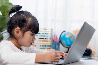 Asyalı liseli kız evde dizüstü bilgisayarla ödevini yapıyor. Çocuklar çalışmak için aletler kullanırlar. Çocuklar için eğitim ve uzak mesafe eğitimi. Karantina sırasında evde eğitim. Evde kal.