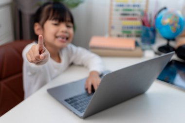 Asyalı liseli kız evde dizüstü bilgisayarla ödevini yapıyor. Çocuklar çalışmak için aletler kullanırlar. Çocuklar için eğitim ve uzak mesafe eğitimi. Karantina sırasında evde eğitim. Evde kal.