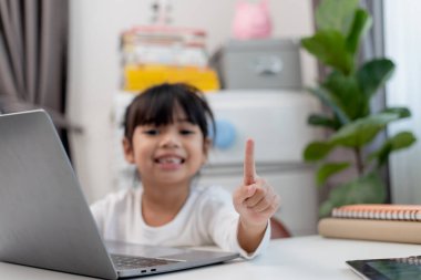 Asyalı liseli kız evde dizüstü bilgisayarla ödevini yapıyor. Çocuklar çalışmak için aletler kullanırlar. Çocuklar için eğitim ve uzak mesafe eğitimi. Karantina sırasında evde eğitim. Evde kal.