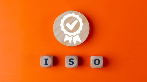 ISO quality control certification concept, top view of wooden blocks with word ISO and certificate sign. on an orange background.