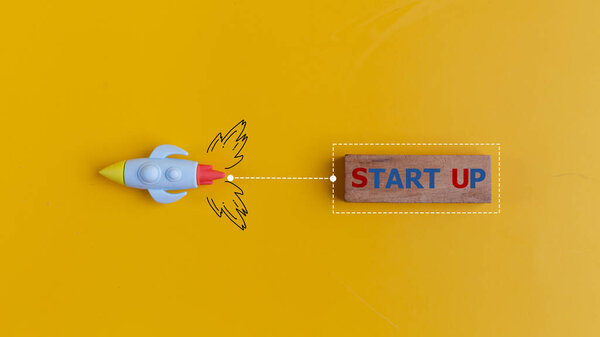 The start up concept with rocket pulls a wooden banner with the word START UP on a yellow background.