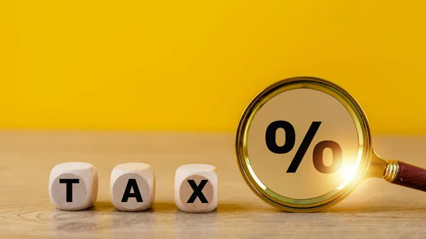 Tax concept with wooden cubes and magnifying glass on a yellow background. Tax payment reminder or annual taxation concept.