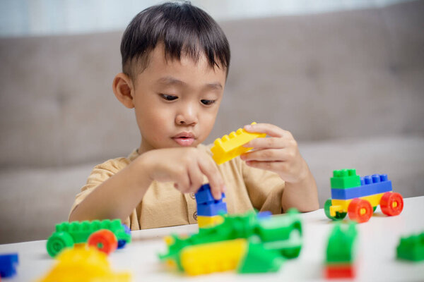 Ребенок играет с красочными игрушечными блоками. Маленький мальчик строит машину из блочных игрушек. Образовательные и творческие игрушки и игры для маленьких детей. 