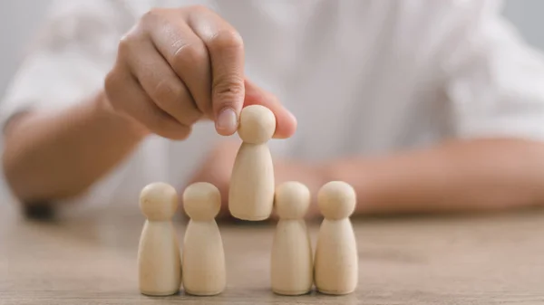 HR manager (human resources) or Employer\'s hand chooses to take person wooden doll. The leader stands out from the crowd. Looking for good worker. HR, HRM, HRD concepts.