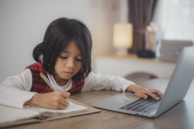 Şirin ve mutlu Asyalı kız çocukları dizüstü bilgisayar kullanıyor, evde online bir e-öğrenme sistemi üzerinden çalışıyorlar..