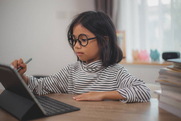 Cute Asian little girl children using a laptop computer, studying through an online e-learning system.