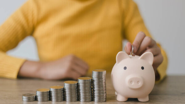 Women put coins in pink piggy banks with increasing coins stacked on the table, Money saving and deposit for investment to get profit and dividend concept.