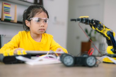 Genç bir kız robot bir oyuncakla masada oturuyor. Güvenlik gözlüğü takıyor ve robota odaklanmış durumda. Sahne, kızın bir bilim ya da mühendislik faaliyetiyle meşgul olduğunu gösteriyor.