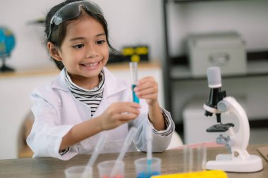 Mikroskobu olan küçük tatlı bir kız su deneyi yapan bir laboratuvar şişesi tutuyor ve okulda bilim adamlarını inceliyor. Eğitim bilimi kavramı.