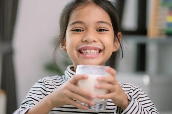 Asian little cute girl drinking milk  Young preschool child girl or daughter stays home with a smiling face, feels happy, and enjoys drinking milk.