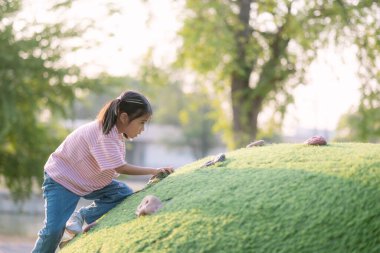 Genç bir kız çimenli bir tepeye tırmanıyor. Sahne parlak ve neşeli, güneş kızın ve çimlerin üzerinde parlıyor. Kız tepeye tırmanırken eğleniyor gibi görünüyor.
