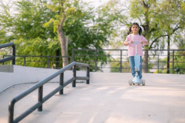 Parkta scooter süren genç bir kız. Özgürlük ve neşe kavramı, kızın dışarıda geçirdiği zamandan zevk alması gibi.