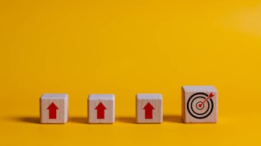 Yukarıyı gösteren bir oka sahip ahşap bir blok sarı bir arka plana yerleştirilir. Arka planda üç tahta blok daha var. Birinin üzerinde kırmızı bir ok var.