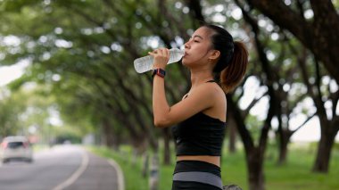 Bir kadın yolda yürürken su içiyor. Sağlık ve zindelik kavramı, kadın yürüyüşü boyunca susuz kalmadan vücuduna özen gösteriyor.
