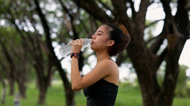 Bir kadın yolda yürürken su içiyor. Sağlık ve zindelik kavramı, kadın yürüyüşü boyunca susuz kalmadan vücuduna özen gösteriyor.