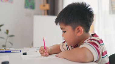 Bir çocuk bir kağıt parçasına pembe bir kalemle yazıyor. O işine odaklanmış ve eğleniyor gibi görünüyor. Sahne penceresi olan bir odada geçiyor.