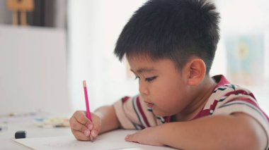 Bir çocuk bir kağıt parçasına pembe bir kalemle yazıyor. O işine odaklanmış ve eğleniyor gibi görünüyor. Sahne penceresi olan bir odada geçiyor.