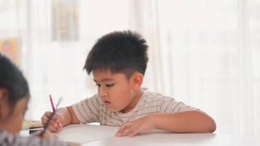 Bir çocuk bir kağıt parçasına pembe bir kalemle yazıyor. O işine odaklanmış ve eğleniyor gibi görünüyor. Sahne penceresi olan bir odada geçiyor.