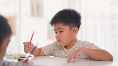 Bir çocuk bir kağıt parçasına pembe bir kalemle yazıyor. O işine odaklanmış ve eğleniyor gibi görünüyor. Sahne penceresi olan bir odada geçiyor.